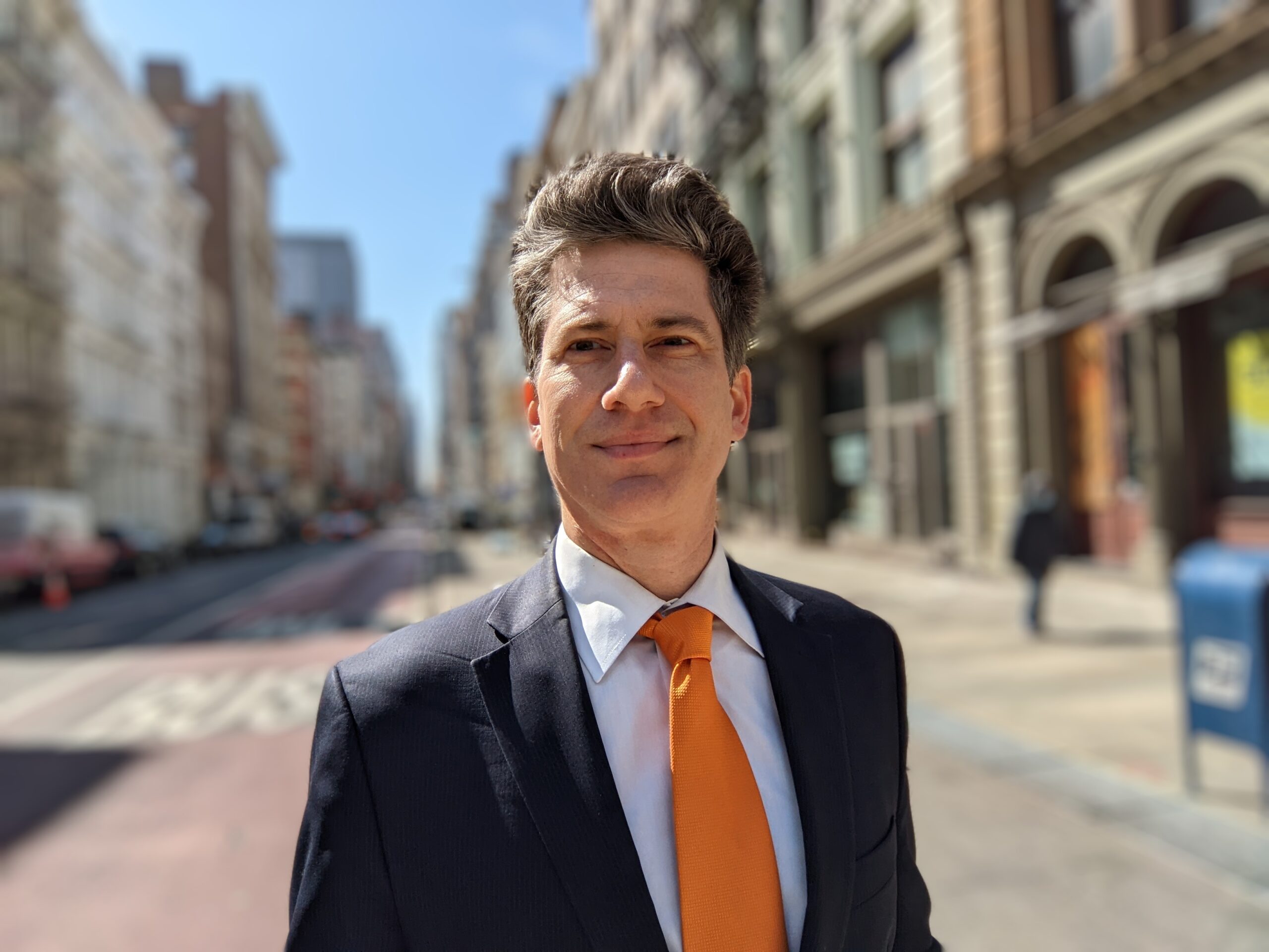 Man in suit with orange tie on sidewalk